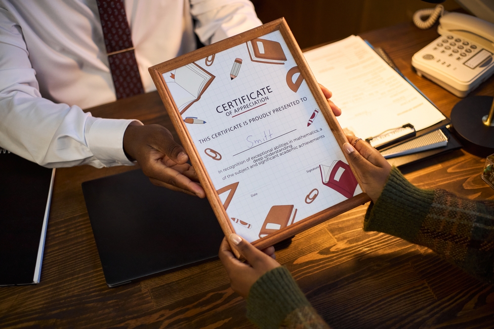 Middle,Aged,Black,Man,Sitting,At,Desk,Handing,Framed,Certificate